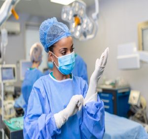 Young female doctor prepares for surgery, wears blue surgical gloves, in a coat and mask